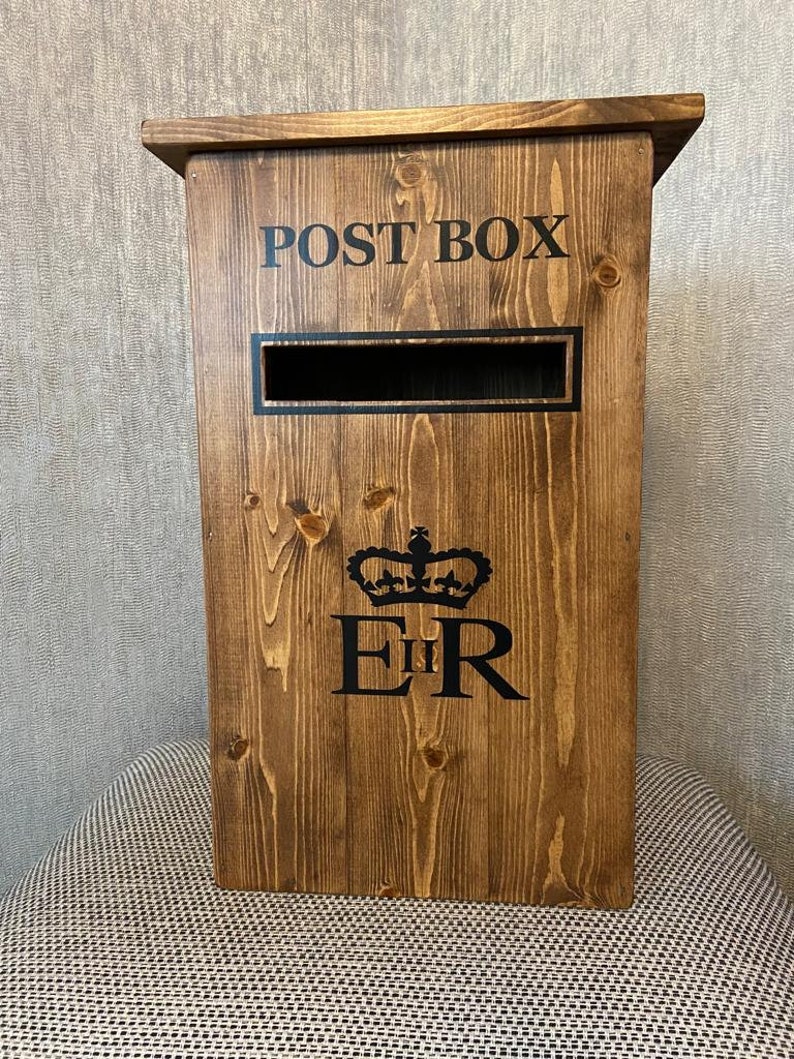 May include: A wooden post box with a slot for mail. The box is painted brown and has the words "POST BOX" printed on the front. The box also has a royal crown and the letters "E II R" printed on the front.