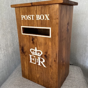 May include: A wooden post box with a white inscription that reads "POST BOX" and a white royal crest with the letters "EIIR".