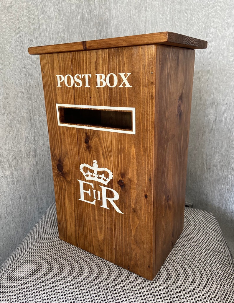 May include: A wooden post box with a white inscription that reads "POST BOX" and a white royal crest with the letters "EIIR".