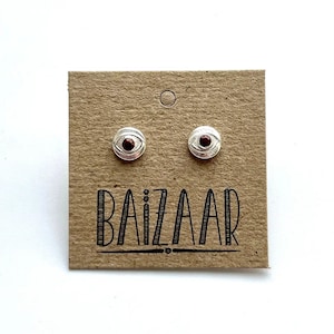 May include: A pair of silver earrings with a red eye design. The earrings are on a brown card with the word "BAIZAAR" printed on it.