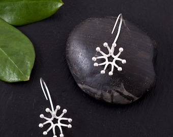 May include: A pair of silver dangle earrings with a starburst design. The earrings are on a black background with a smooth, gray stone.