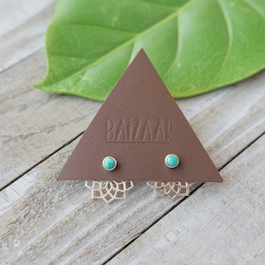 May include: A pair of silver earrings with turquoise stones and a delicate mandala design. The earrings are displayed on a brown triangular card with the word "BAZAAR" printed on it.