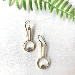 May include: A pair of gold earrings with a geometric design. Each earring features a small blue gemstone set in a circle.