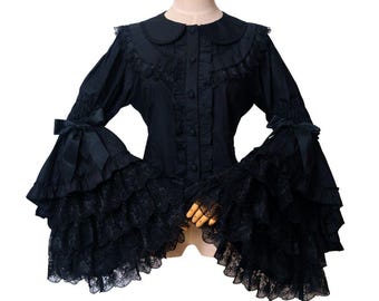 May include: Black blouse with a Peter Pan collar, button-up front, and long sleeves. The sleeves feature bows at the cuffs and dramatic, layered lace ruffles. The blouse has a fitted bodice and a flared, ruffled hemline. The Night Whisper logo is at the bottom.