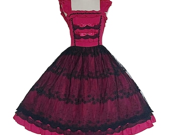 May include: A sleeveless, pink dress with a black lace overlay and a layered skirt. The bodice features a square neckline and a ribbon detail. The dress is on a white mannequin.