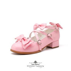 Könnte beinhalten: Rosa Lackleder Mary Jane Schuhe mit Schleifenakzenten. Die Schuhe haben einen kleinen Blockabsatz und herzförmige Schnallen. Das Design umfasst eine große Schleife auf der Zehe und kleinere Schleifen an den Riemen.