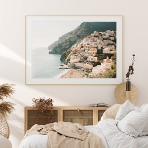 May include: A framed photograph of a coastal town built into a hillside. The town is a mix of white and pastel-colored buildings with a few trees and a small beach in the foreground. The sea is a light blue color and the sky is a pale blue.