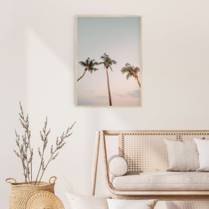 May include: A framed print of three palm trees against a light blue sky with a pink sunset in the background.