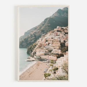May include: A photograph of a coastal town built into a hillside, with a sandy beach and clear blue water in the foreground. The town is a mix of white and pastel-colored buildings, with lush green vegetation growing on the hillside.