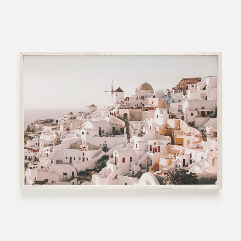 May include: A panoramic view of a whitewashed village perched on a cliffside, with a windmill and a domed church in the background. The buildings are painted in shades of white and beige, with red accents. The sky is a soft blue, and the sea is visible in the distance.