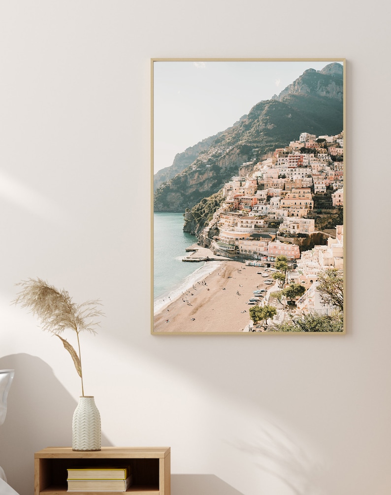 May include: A photograph of a colorful town built on a cliffside overlooking a sandy beach and the ocean. The town is a mix of pastel colors, with white buildings and terracotta roofs. The beach is empty, with a few people walking along the shore.
