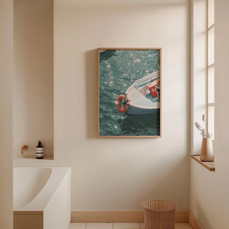 Op de afbeelding: Een ingelijste foto van een kleine witte boot met een oranje reddingsboei die drijft in turquoise water met zonlicht dat reflecteert op het oppervlak.