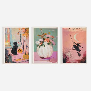 Pode incluir: Três pinturas emolduradas com um tema de Halloween. A primeira pintura mostra um gato preto sentado ao lado de uma abóbora talhada. A segunda pintura mostra um vaso de abóbora branco com flores rosa e brancas. A terceira pintura mostra uma silhueta de uma bruxa voando em uma vassoura.