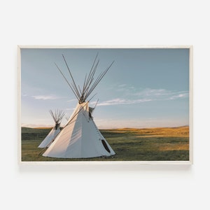 May include: Two white teepees stand in a grassy field under a blue sky with white clouds. The teepees are made of canvas and have wooden poles.