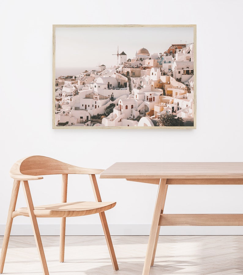 May include: A framed photograph of a whitewashed village with a windmill on a hilltop. The village is built on a cliff overlooking the sea. The photo is in a light wood frame.