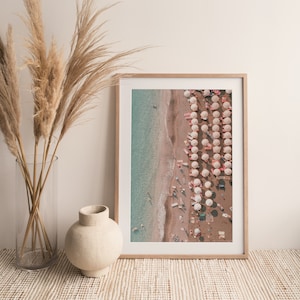 Peut inclure: Une photographie encadr&eacute;e d'une sc&egrave;ne de plage avec des parasols blancs et une eau turquoise. La photo est prise d'en haut, montrant une longue rang&eacute;e de parasols et des gens sur la plage.