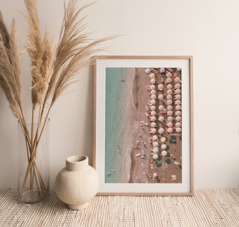 Peut inclure: Une photographie encadr&eacute;e d'une sc&egrave;ne de plage avec des parasols blancs et une eau turquoise. La photo est prise d'en haut, montrant une longue rang&eacute;e de parasols et des gens sur la plage.