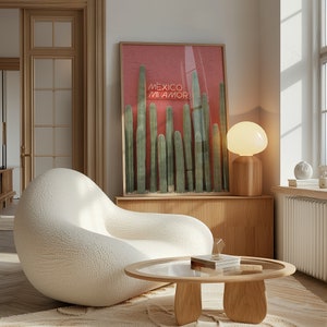May include: A white, plush armchair with a rounded shape sits in a living room with a wooden coffee table and a framed print of cacti with the text "Mexico Mi Amor" on a red background. A lamp with a white globe sits on a wooden shelf.