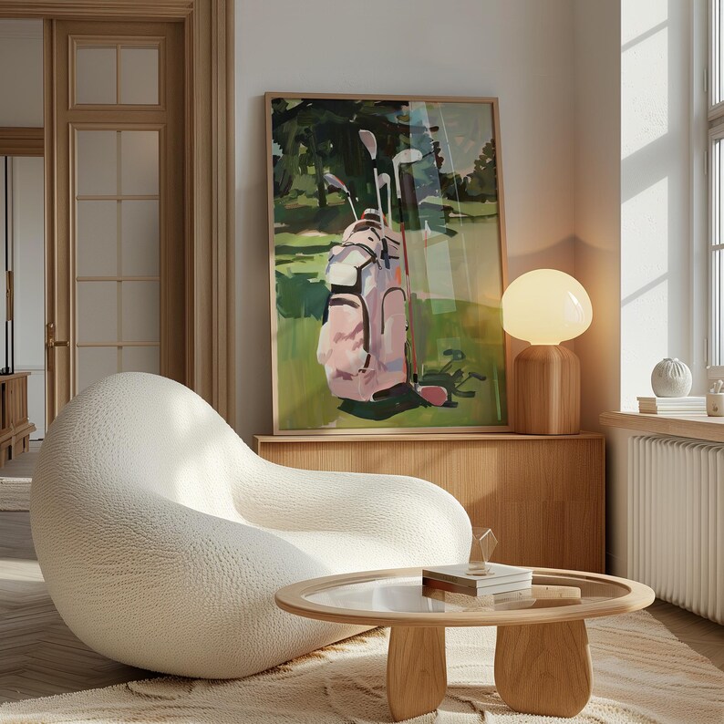 May include: A framed art print showing a golf bag with clubs on a green golf course. The golf bag is pink and white. The artwork is displayed above a wooden cabinet, next to a white, rounded chair and a round wooden coffee table.