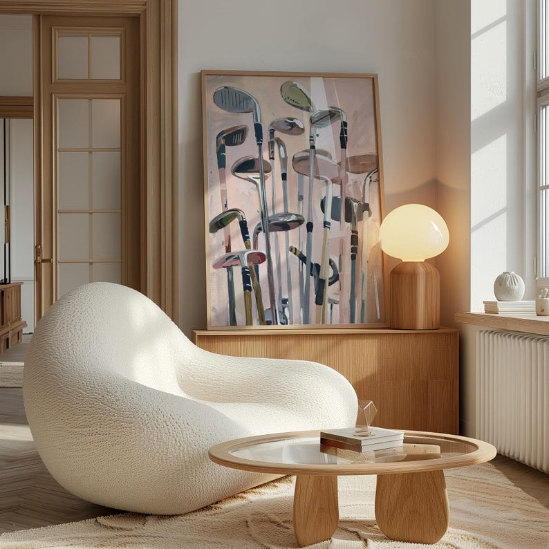 May include: An interior scene featuring a large, abstract painting of golf clubs in a wooden frame. A white, textured, curved armchair and a round wooden coffee table with a glass top are in the foreground. A wooden cabinet and a spherical lamp are also visible.