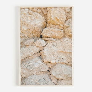 May include: A close-up of a wall made of rough, beige-coloured stones. The stones are stacked on top of each other, creating a textured surface.