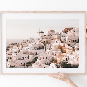 May include: A framed photograph of a whitewashed village with a windmill on a hilltop. The village is built on a cliff overlooking the sea. The photo has a warm, golden light.