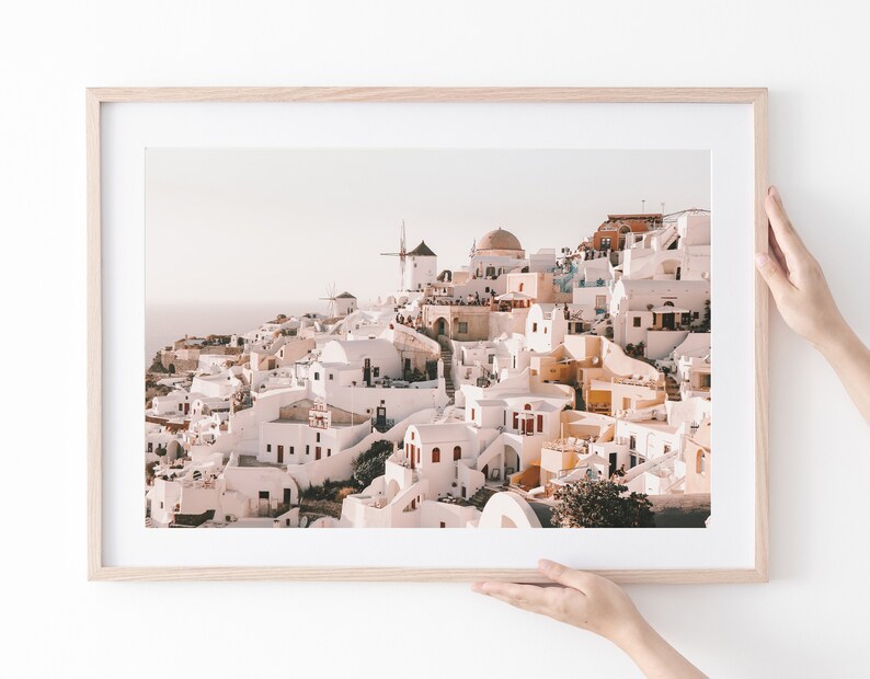 May include: A framed photograph of a whitewashed village with a windmill on a hilltop. The village is built on a cliff overlooking the sea. The photo has a warm, golden light.