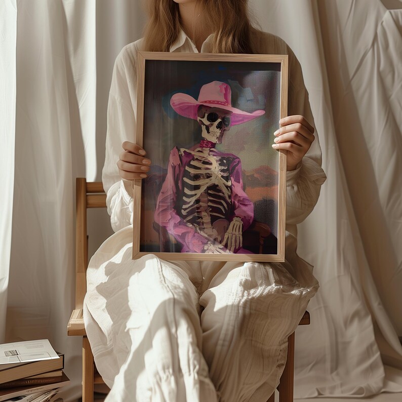 May include: A framed painting of a skeleton wearing a pink cowboy hat and a purple shirt. The skeleton is sitting in a chair with its hands resting on its lap.