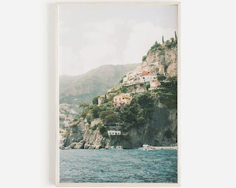 Könnte beinhalten: Ein Foto eines Dorfes an einem steilen Abhang in Italien. Das Dorf ist in den Hang eines steilen Kliffs gebaut, mit Häusern, die den Hang hinunterkaskaden. Das Wasser ist tiefblau und der Himmel ist hellblau. Das Bild wurde von einem Boot im Wasser aus aufgenommen, mit Blick auf das Dorf.