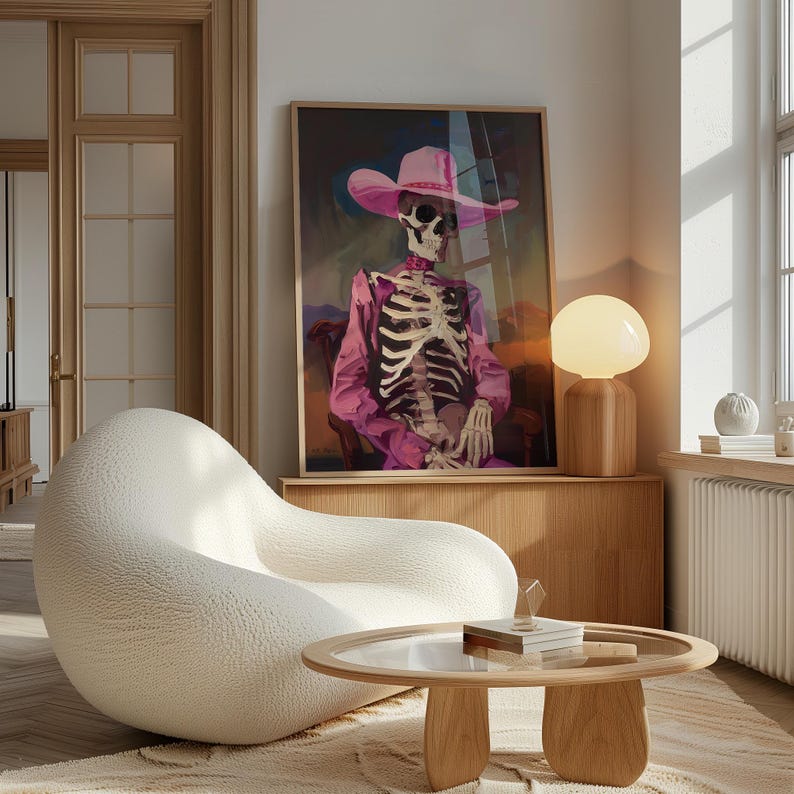 May include: A white, textured armchair with a round, glass-top coffee table in front of it. A framed print of a skeleton wearing a pink cowboy hat and shirt hangs on the wall behind the armchair. A white lamp with a round, white shade sits on a wooden shelf.