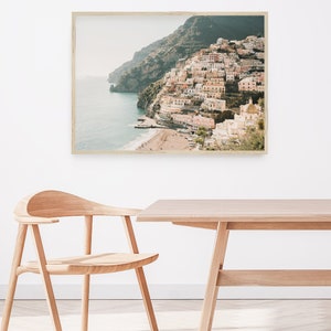 May include: A framed photograph of a coastal town built on a hillside overlooking a blue ocean. The town is a mix of white and pastel-colored buildings with a few green trees. The photo is taken from a high angle, giving a panoramic view of the town and the ocean.