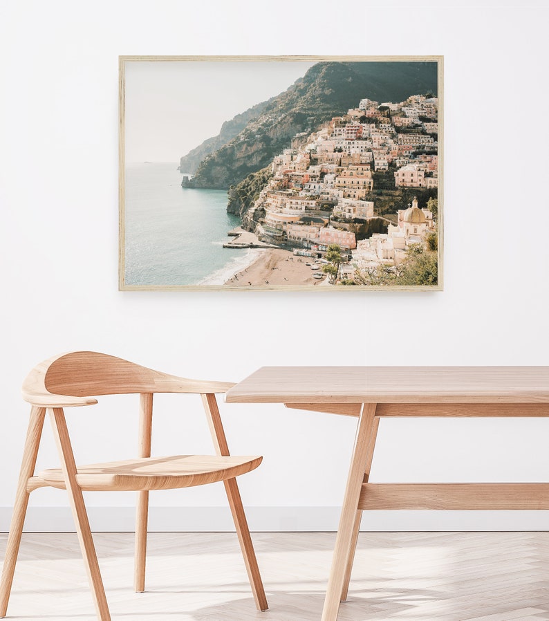 May include: A framed photograph of a coastal town built on a hillside overlooking a blue ocean. The town is a mix of white and pastel-colored buildings with a few green trees. The photo is taken from a high angle, giving a panoramic view of the town and the ocean.