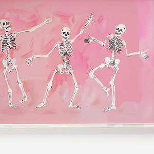 May include: Three white skeletons dancing on a pink background. The skeletons are drawn in a simple style with black lines and are posed in a playful and energetic way.