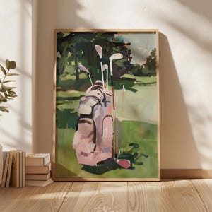 May include: A framed art print showing a golf course. The image features a pink golf bag with clubs on a green fairway, with trees in the background. The painting has a soft, impressionistic style, with visible brushstrokes and a muted colour palette.