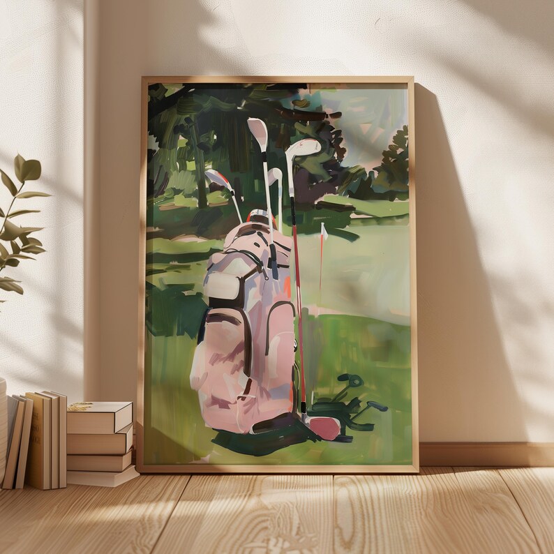 May include: A framed art print showing a golf course. The image features a pink golf bag with clubs on a green fairway, with trees in the background. The painting has a soft, impressionistic style, with visible brushstrokes and a muted colour palette.