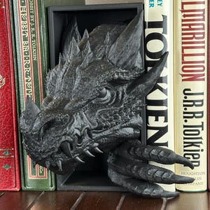 May include: Black dragon head bookends. The dragon is sculpted in a realistic style with sharp teeth and claws. The bookends are made of a durable material and are perfect for holding books or other items.