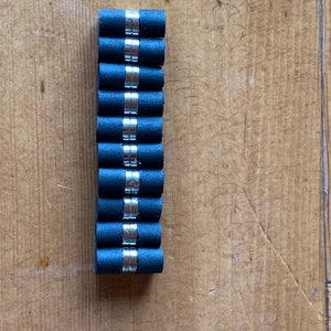 May include: A stack of ten black rubber and silver magnetic cylinder-shaped bottle stoppers.