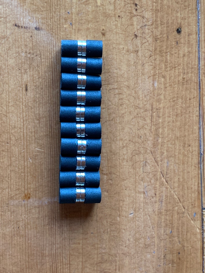 May include: A stack of ten black rubber and silver magnetic cylinder-shaped bottle stoppers.