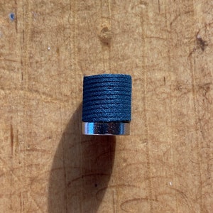 May include: A black and silver knob with a textured surface.