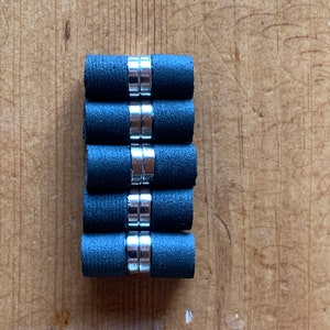 May include: A stack of six black and silver magnetic cylinder-shaped bottle stoppers.