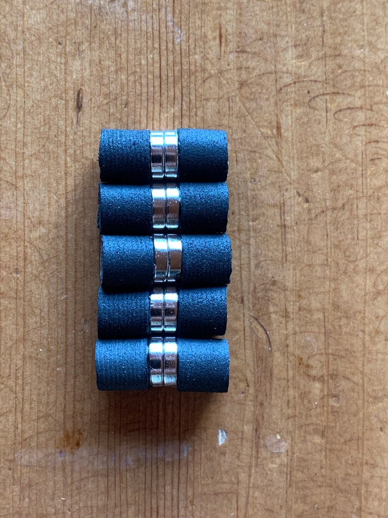 May include: A stack of six black and silver magnetic cylinder-shaped bottle stoppers.
