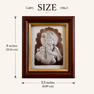 May include: Silver-coloured framed artwork of a deity playing a flute. The frame is dark brown with a gold inner border. The artwork is 10.16 cm tall and 8.89 cm wide. The word "SIZE" is at the top.