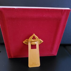 May include: A red velvet picture frame with a gold-coloured easel back. The frame has a simple design and a classic look. The easel back is attached to the frame with a hinge and can be used to display the frame on a table or shelf.