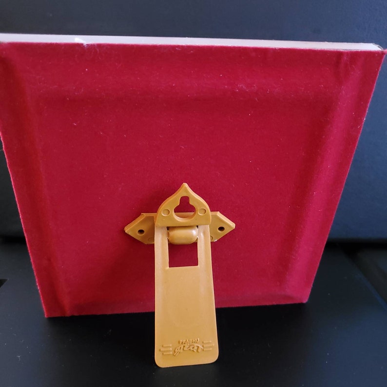 May include: A red velvet picture frame with a gold-coloured easel back. The frame has a simple design and a classic look. The easel back is attached to the frame with a hinge and can be used to display the frame on a table or shelf.