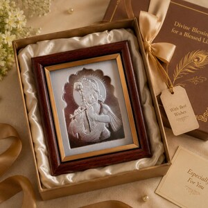 May include: A silver religious icon in a dark brown framed, presented in a gift box with a satin lining. The box is brown with a decorative ribbon and a tag that reads "With Best Wishes". The image is of a deity.
