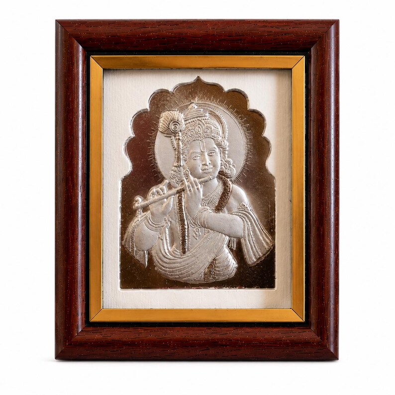 May include: A framed silver relief sculpture of a figure playing a flute, set against a white background. The artwork is framed in a dark brown wood frame with a gold inner border. The figure has a halo.