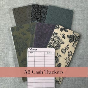 May include: A set of A6 cash trackers featuring various patterns including black skulls, dark floral motifs, and geometric designs. One tracker is white with a printed table containing the headers Category, Date, +/-, and Balance.