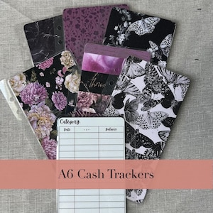 May include: A collection of A6 cash trackers with various designs. The trackers feature floral, butterfly, and marble patterns in shades of purple, black, and white. One tracker has a grid for tracking expenses. The text "A6 Cash Trackers" is displayed.