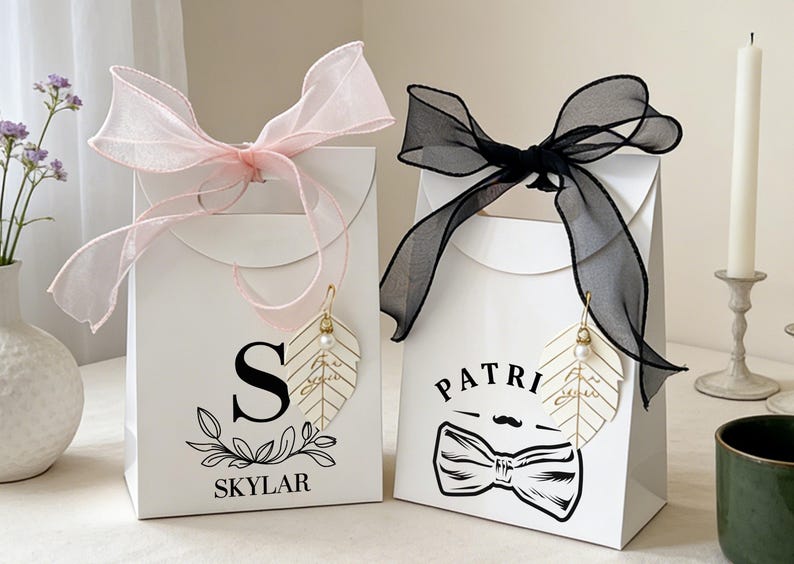 May include: Two white gift bags with decorative bows. One has a pink bow, the other a black bow. Each bag has a leaf-shaped charm and personalized text. One says "Skylar" and the other says "Patri".