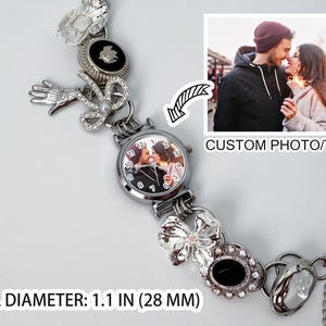 May include: A silver-toned watch with a custom photo on the dial, surrounded by decorative charms. The watch features a dial diameter of 1.1 inches (28 mm) and includes the text "CUSTOM PHOTO/TEXT". The watch is adorned with various embellishments.